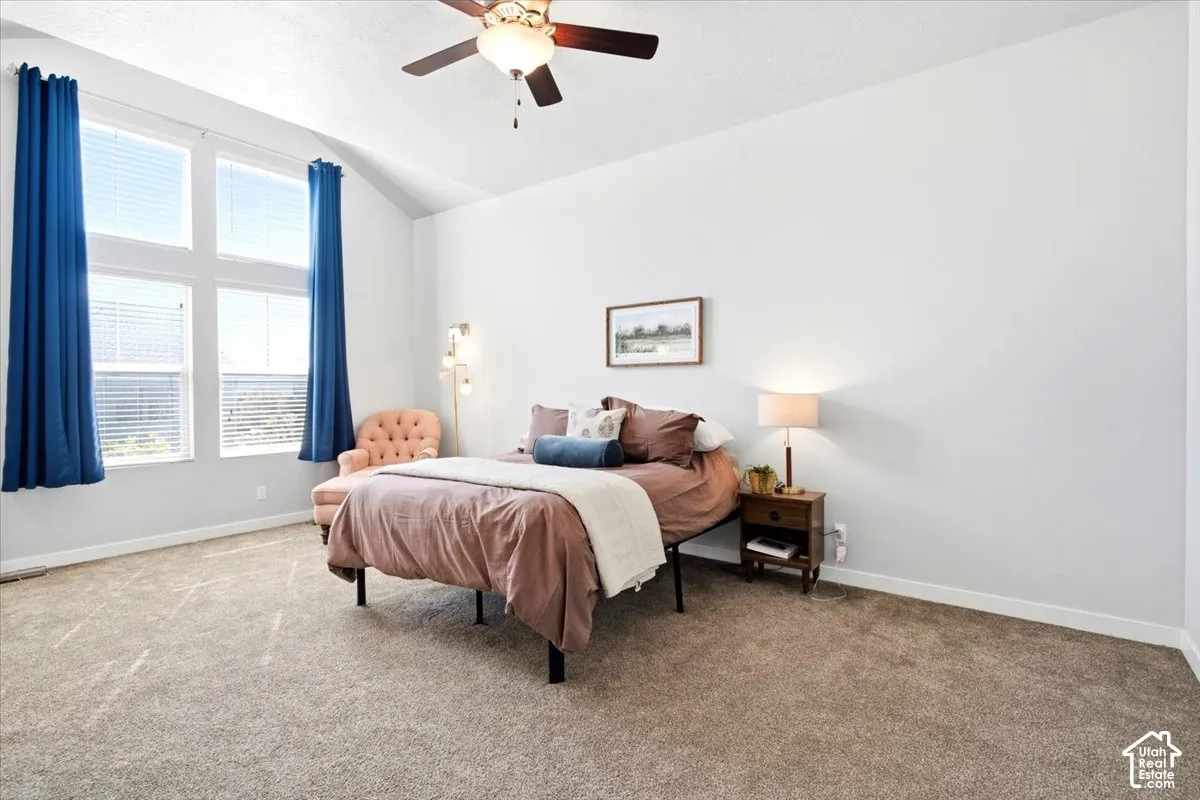 Vaulted ceiling, ceiling fan, large windows, blinds, and light-toned carpeting