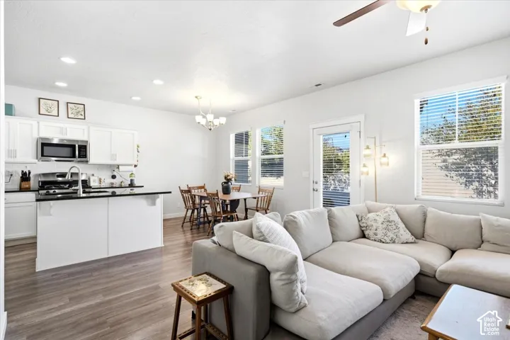 Open-concept living area with wood-finish flooring, white cabinetry, stainless steel appliances, and ceiling fan