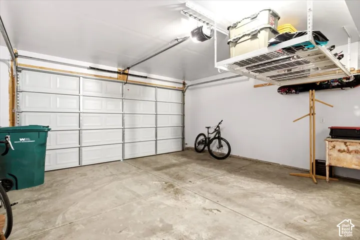 Attached garage with a white panel door, concrete flooring, and an overhead storage rack