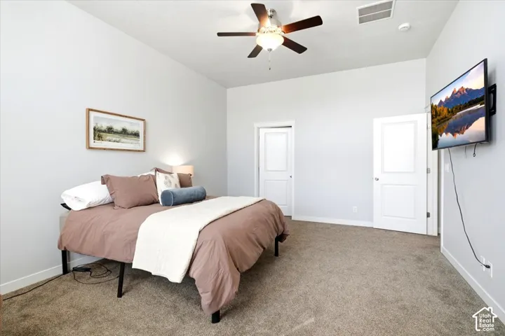 Carpeted room featuring a ceiling fan with integrated lighting, two panel doors, and a wall-mounted television