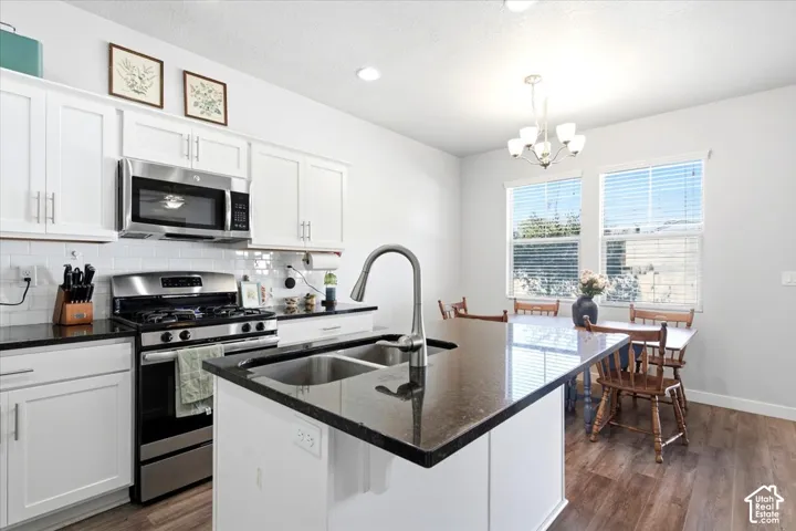 Kitchen featuring white cabinetry, stainless steel appliances, dark countertops, and wood-finish flooring