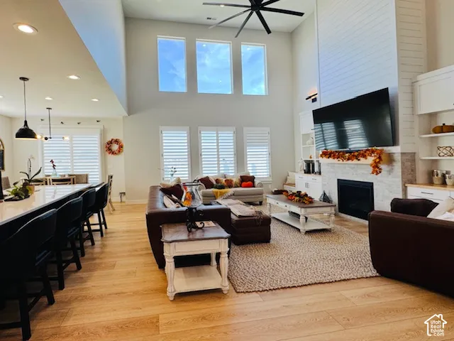 Vaulted ceiling with a large ceiling fan, natural wood-finish flooring, fireplace with a tiled surround, built-in shelving, and an extended kitchen island with pendant lighting