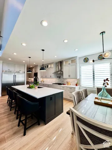 Spacious kitchen featuring a dark-toned island with seating, light wood-finish flooring, recessed lighting, and stainless steel appliances