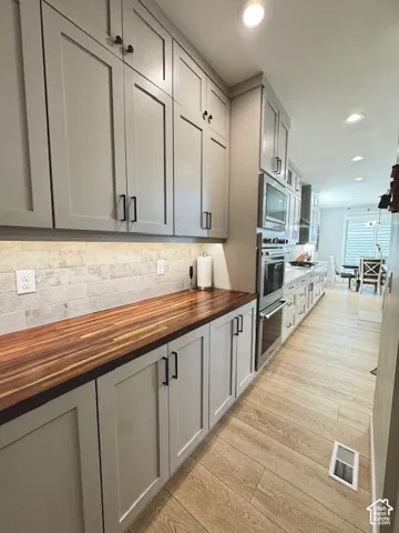 Contemporary kitchen featuring light gray shaker cabinetry, wood-finish countertops, subway tile backsplash, and light wood-look flooring
