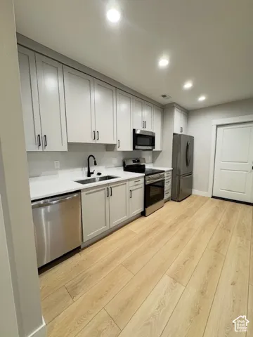 Modern kitchen featuring light wood-finish flooring, white cabinetry, stainless steel appliances, a black sink, and recessed lighting
