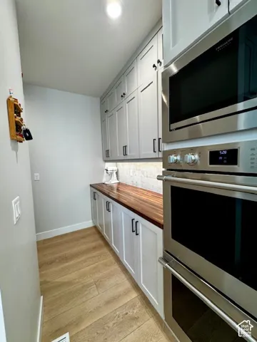 Recessed ceiling lighting illuminates extensive cabinetry with black hardware, wood-finish flooring, and a built-in stainless steel microwave and oven