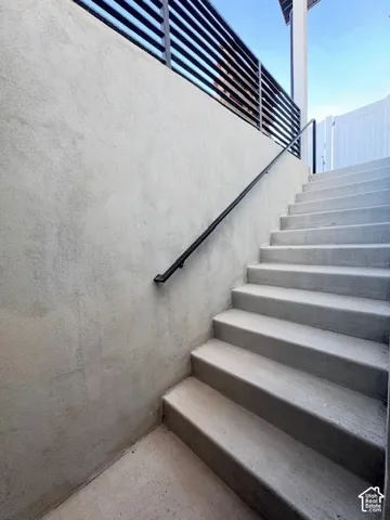 Concrete stairs with a black metal handrail and a textured retaining wall
