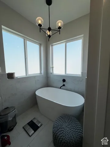 Freestanding soaking tub with a wall-mounted matte black faucet, surrounded by tiled walls