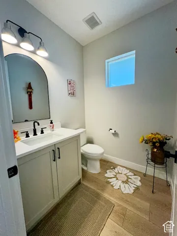 Wood-finish flooring, light-toned vanity with integrated sink, arched mirror, matte black fixtures, and a high-set window