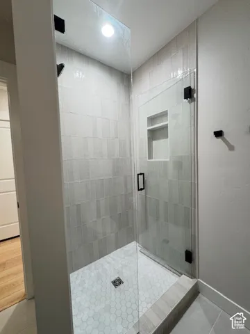 Glass-enclosed shower with a recessed shelf, hexagonal tile flooring, vertically-stacked wall tile, and matte black hardware