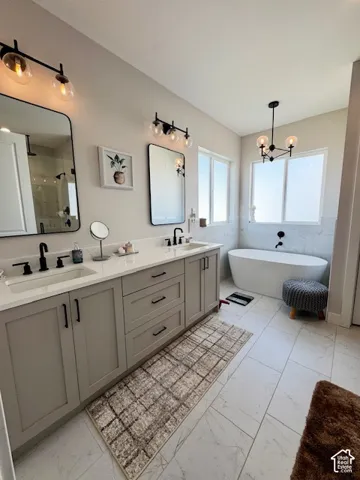 Dual vanity with white countertops and matte black fixtures, integrated freestanding bathtub, large format tile flooring, and multiple window features