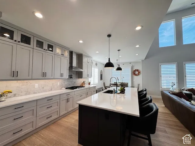 Kitchen featuring light gray cabinetry, white countertops, stainless steel range hood, stone tile backsplash, and wood-finish flooring
