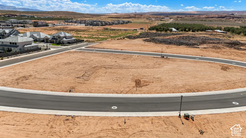 Expansive land parcel featuring paved roads, concrete curbing, and existing residential structures in the background