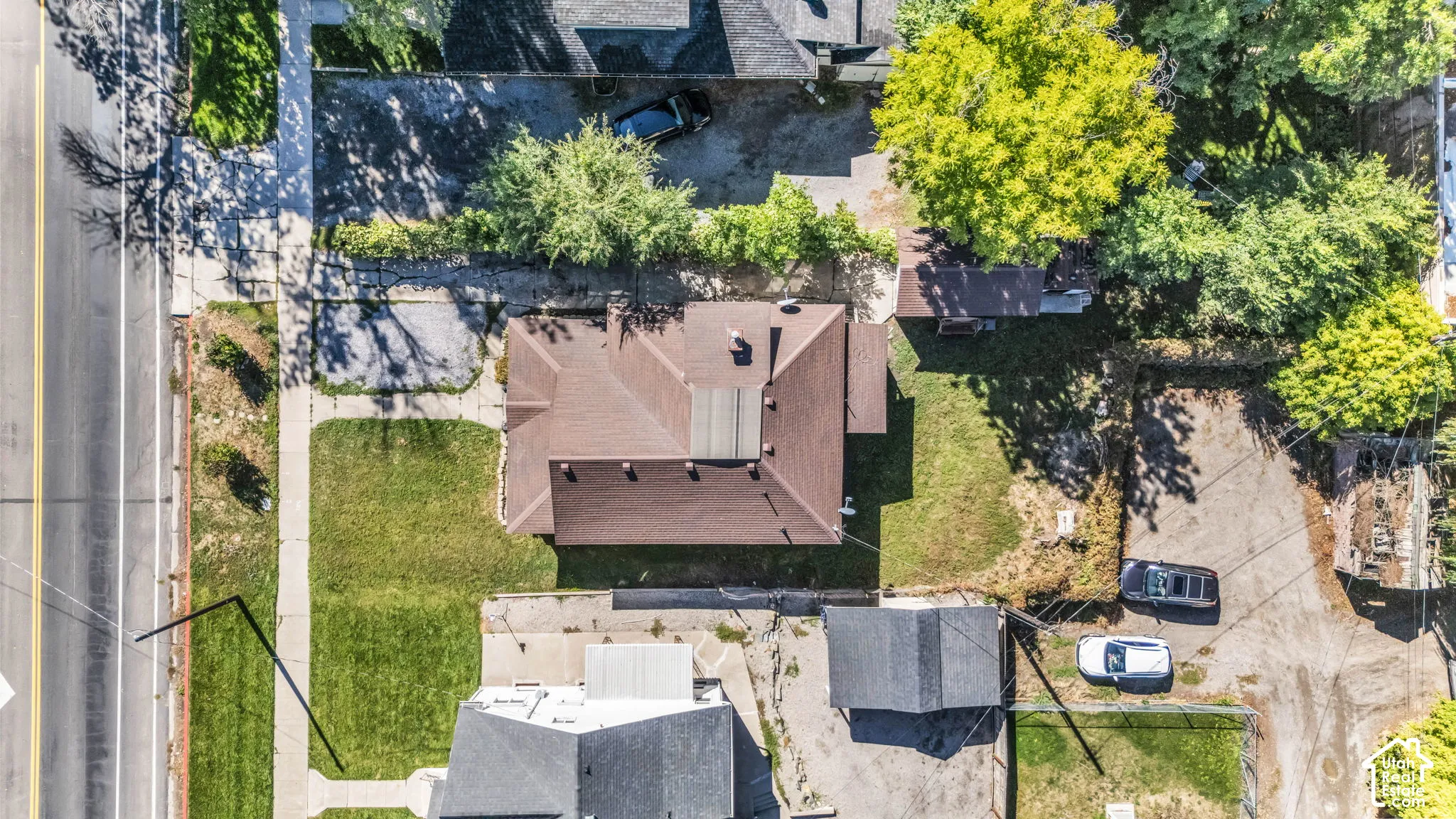 Pitched roof structure with mature trees, a well-maintained lawn, and a sidewalk