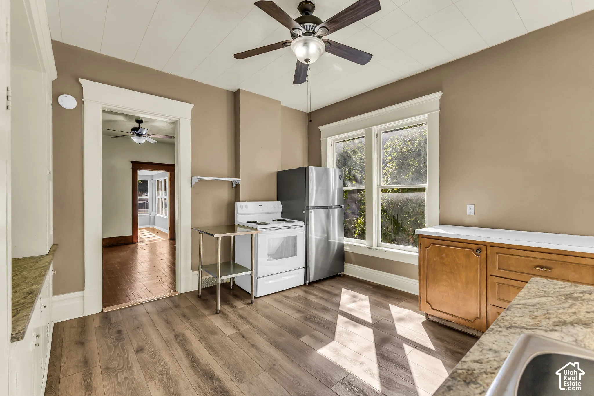 Wood-finish flooring, ceiling fan with integrated lighting, stainless steel refrigerator, white range, and a built-in sink with granite-look countertop