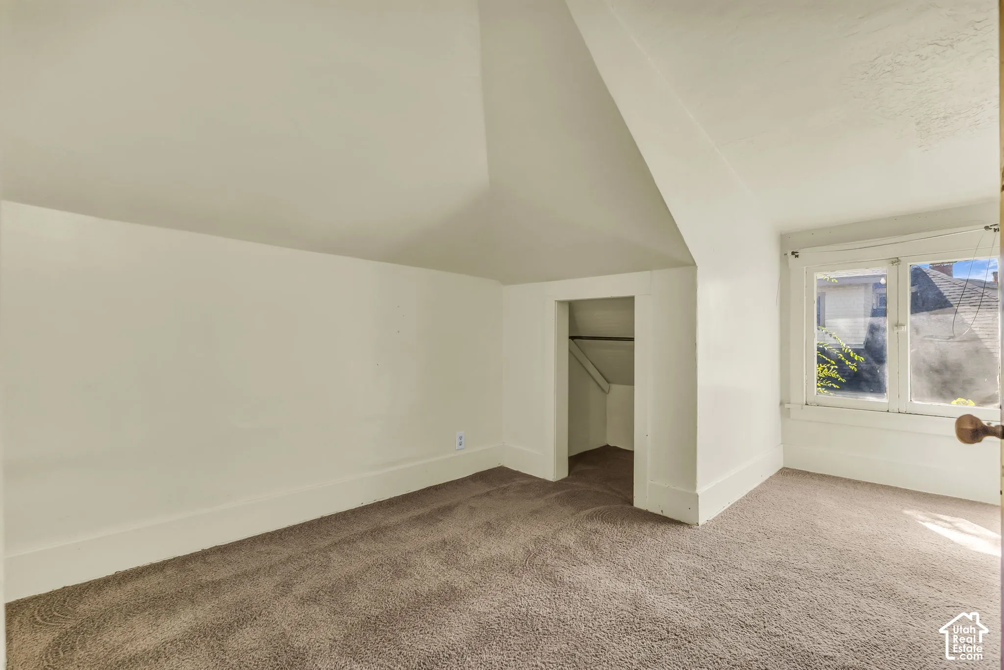 Sloped ceiling featuring a built-in closet with hanging rod, brown carpet flooring, and a single window with white trim