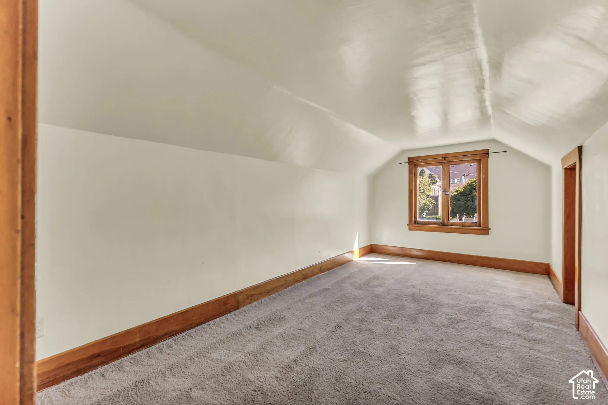 Sloped ceilings, window with wood trim, wood-finish door frame, wood-finish baseboard, and gray carpeting
