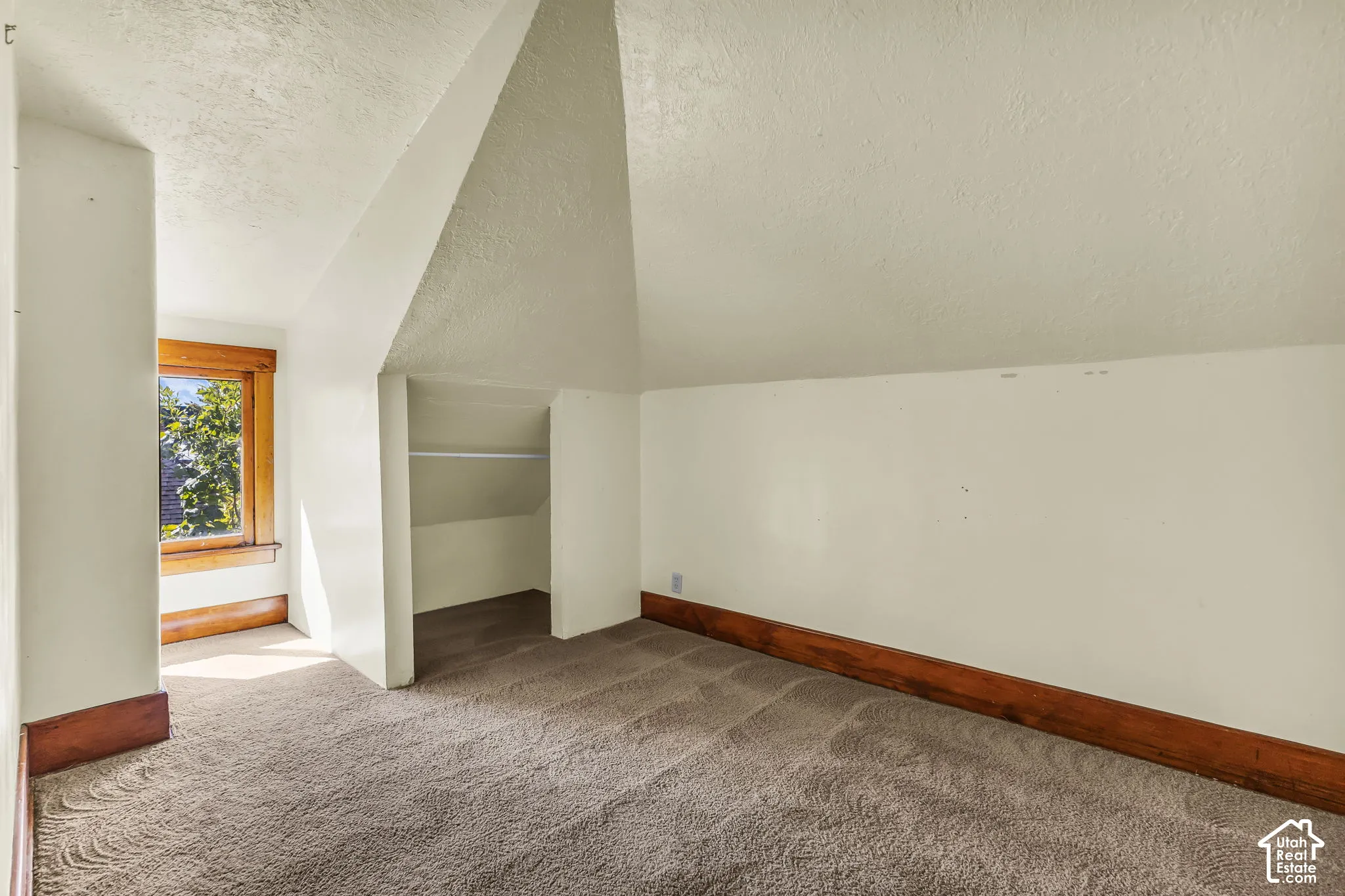Sloped ceiling room featuring a window with wood trim, built-in shelving, carpet flooring, and painted walls