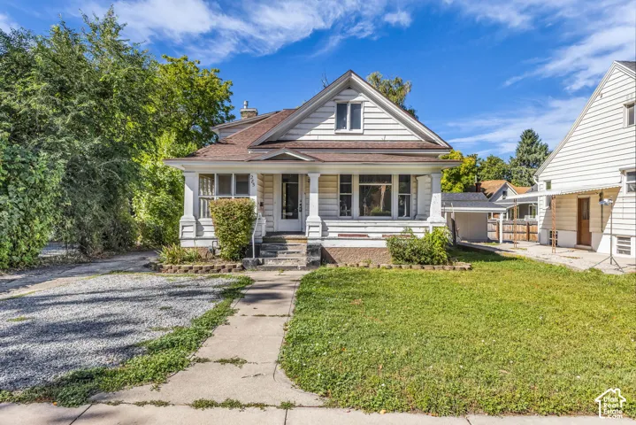 Gable roofline, white siding exterior, covered porch with columns, front yard with green lawn, and gravel driveway