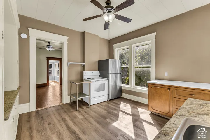 Wood-finish flooring, ceiling fan with integrated lighting, stainless steel refrigerator, white range, and a built-in sink with granite-look countertop
