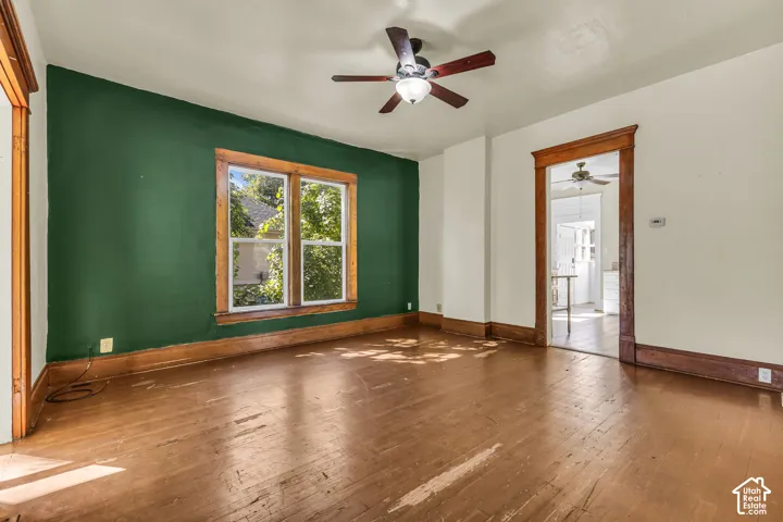 Hardwood-finish flooring, wood-framed window, wooden trim, and a ceiling fan with integrated lighting