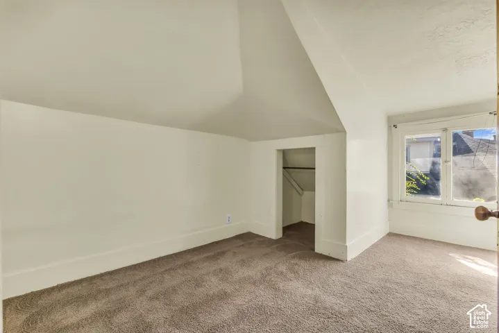 Sloped ceiling featuring a built-in closet with hanging rod, brown carpet flooring, and a single window with white trim