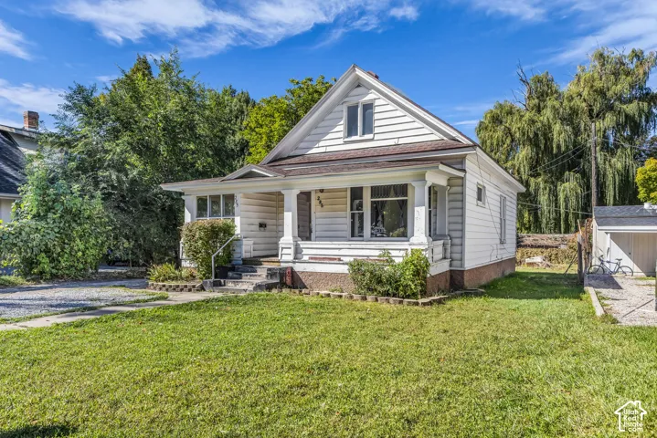 Gable-front home featuring a covered front porch with pillars, white siding, and a brown roof