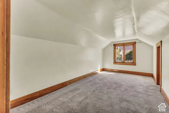 Sloped ceilings, window with wood trim, wood-finish door frame, wood-finish baseboard, and gray carpeting