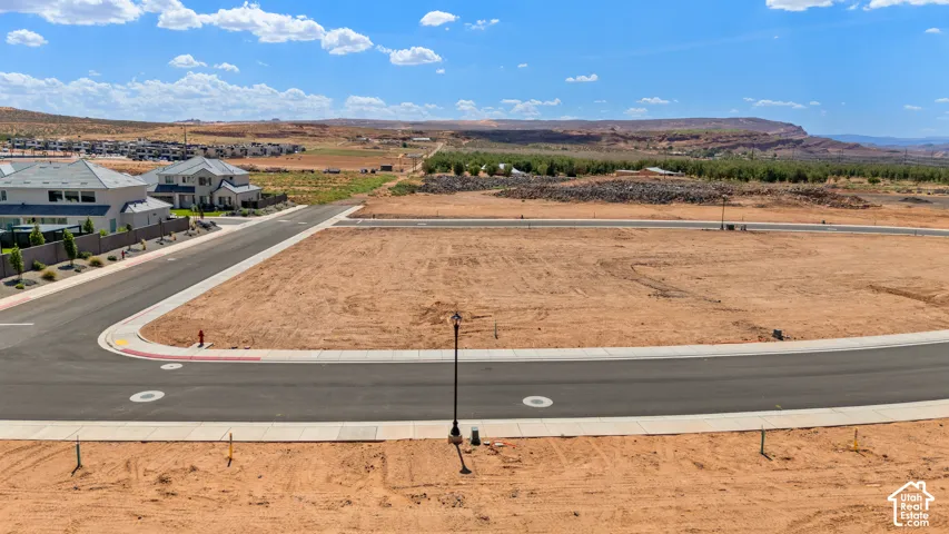 Expansive undeveloped lot featuring a paved street with curbing, street lamp, and distant mountainous terrain