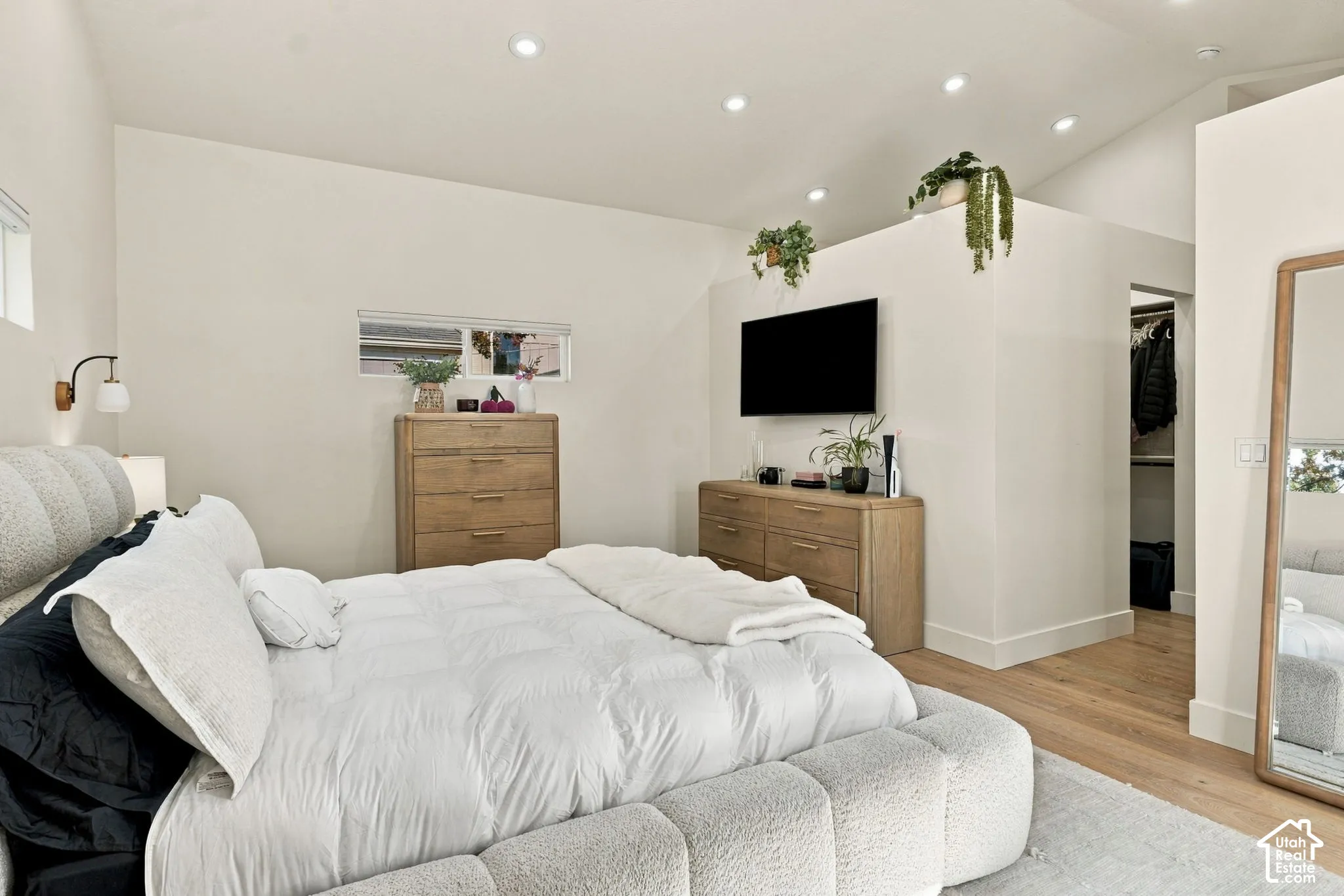 Vaulted ceiling with recessed lighting, light wood-finish flooring, two horizontal windows, and a built-in closet with shelving