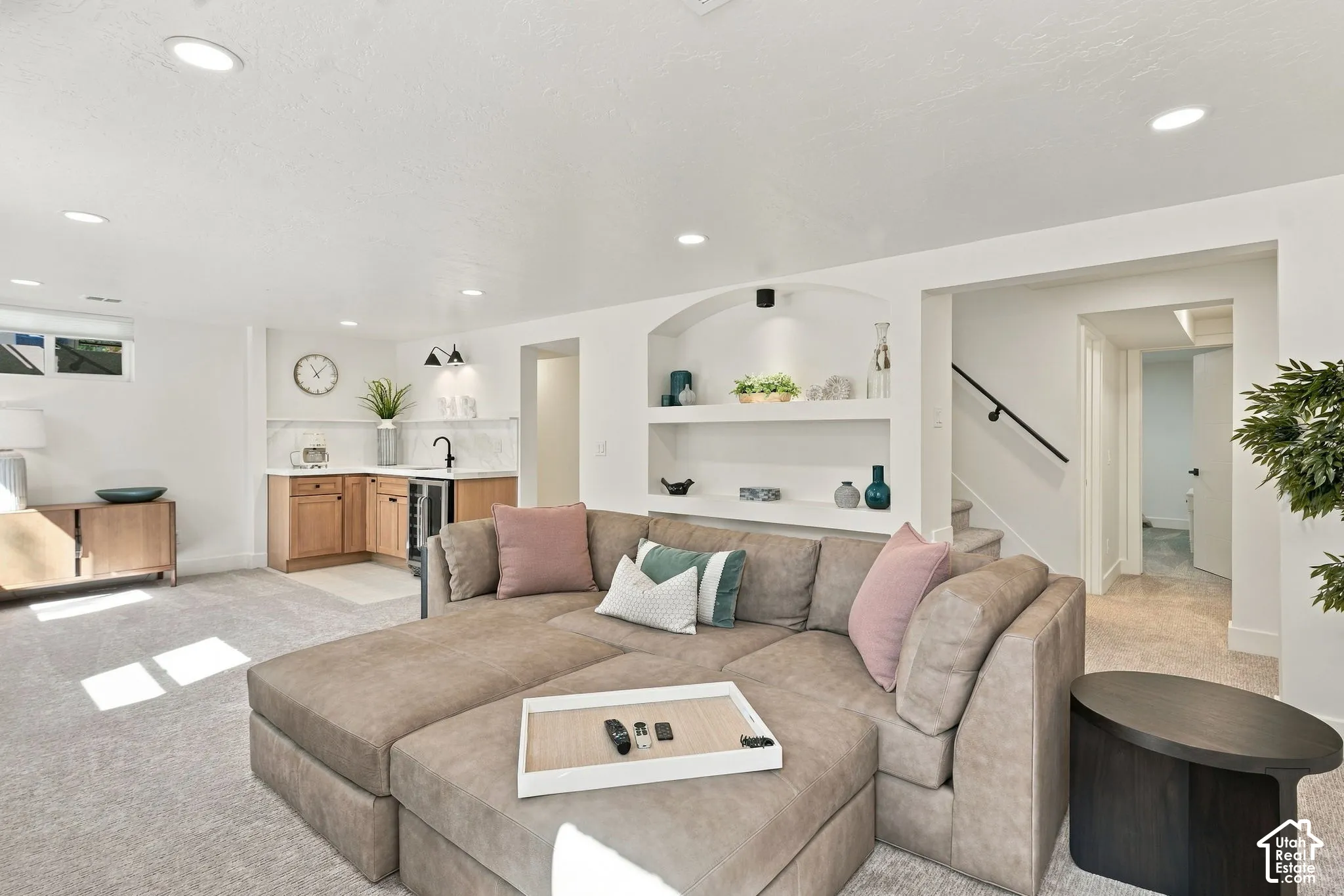 Recessed lighting throughout, built-in shelving with accent lighting, and a wet bar featuring light wood cabinetry