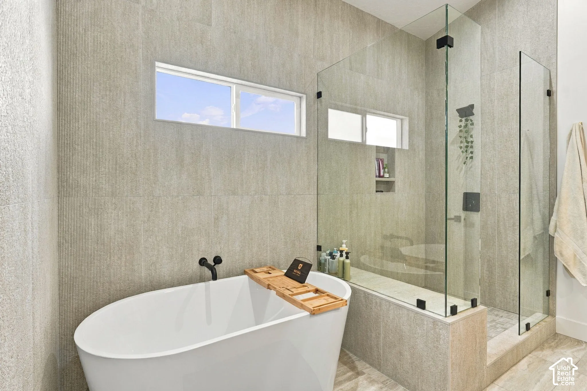 Freestanding soaking tub with matte black fixtures, full-height wall tiling, and a glass-enclosed shower with a built-in niche