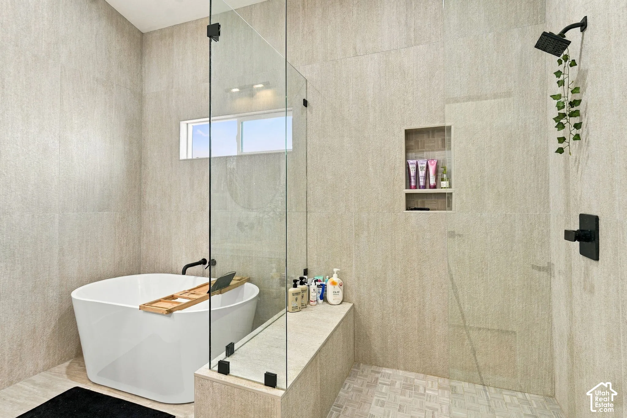 Freestanding soaking tub with matte black fixtures, glass-enclosed shower, tiled shower bench, and recessed shower niche