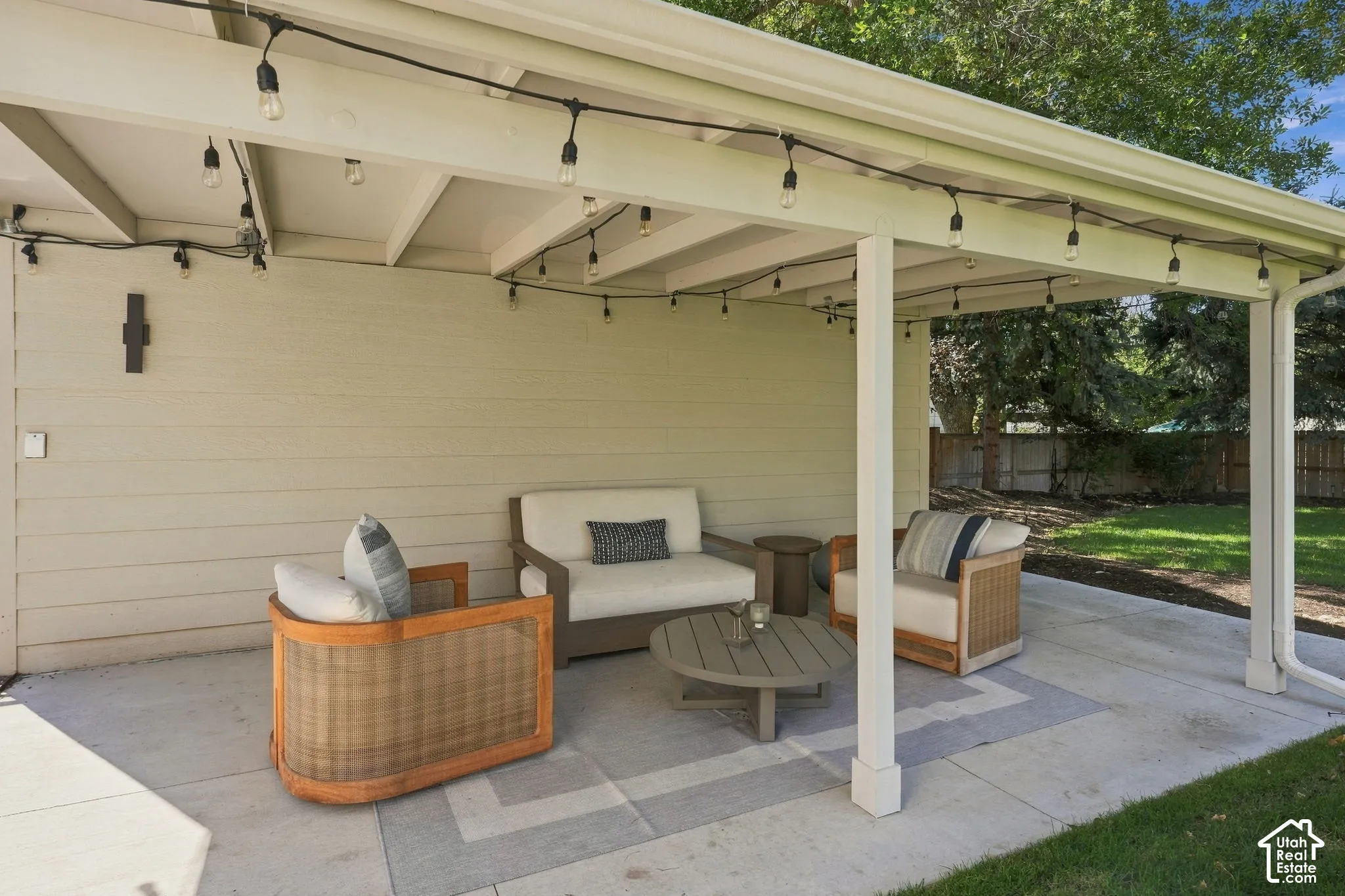 Covered patio featuring string lighting, concrete flooring with a geometric pattern, and an exterior wall-mounted light fixture
