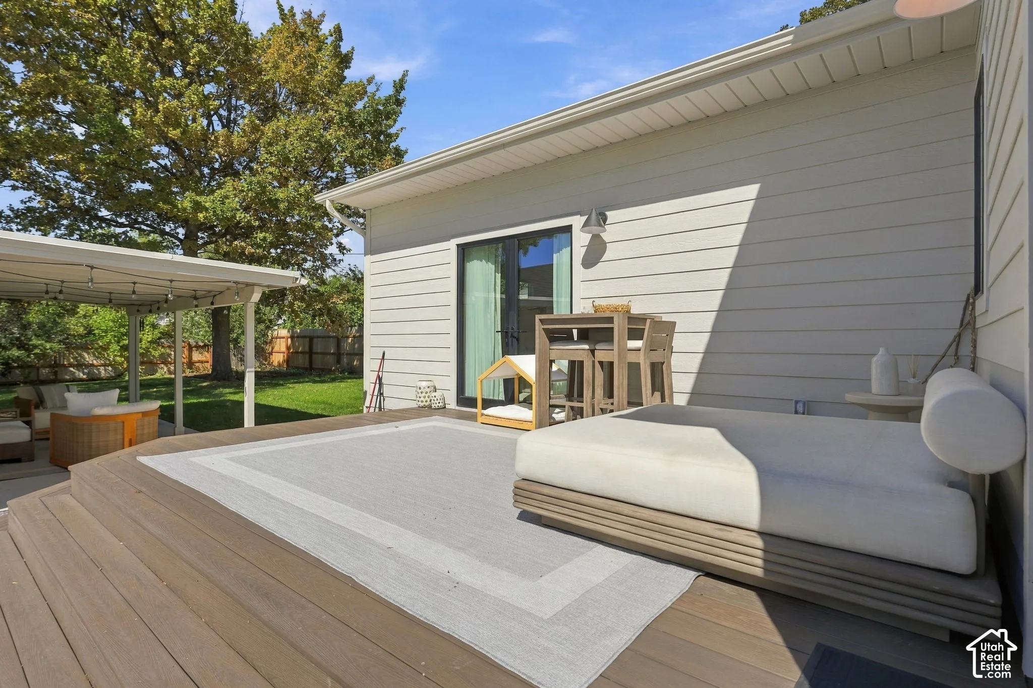 Expansive wood-finish deck with integrated seating, featuring a sliding glass door and a covered patio area
