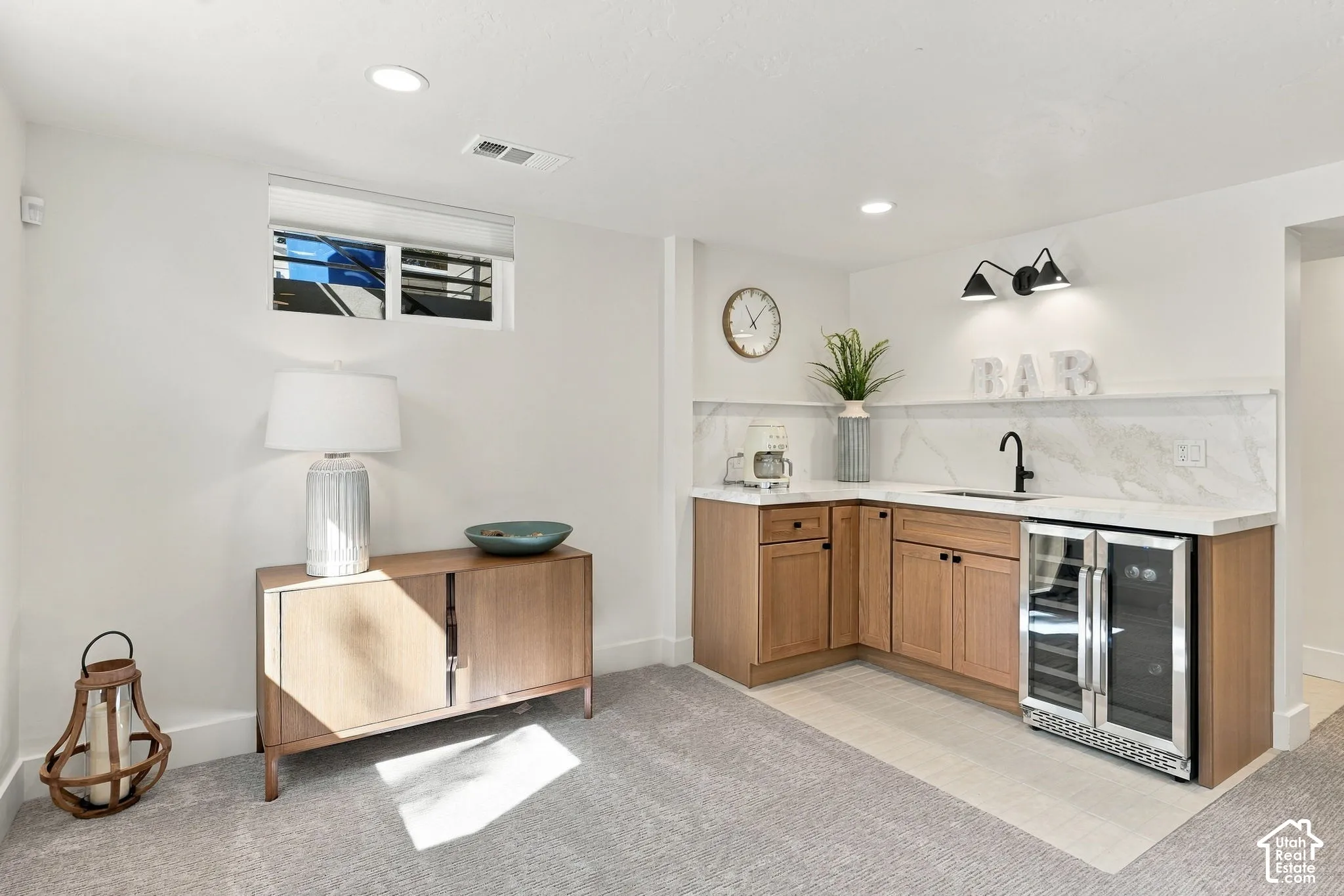 L-shaped wet bar featuring wood-finish cabinetry, a single basin sink with a matte black faucet, and a beverage cooler