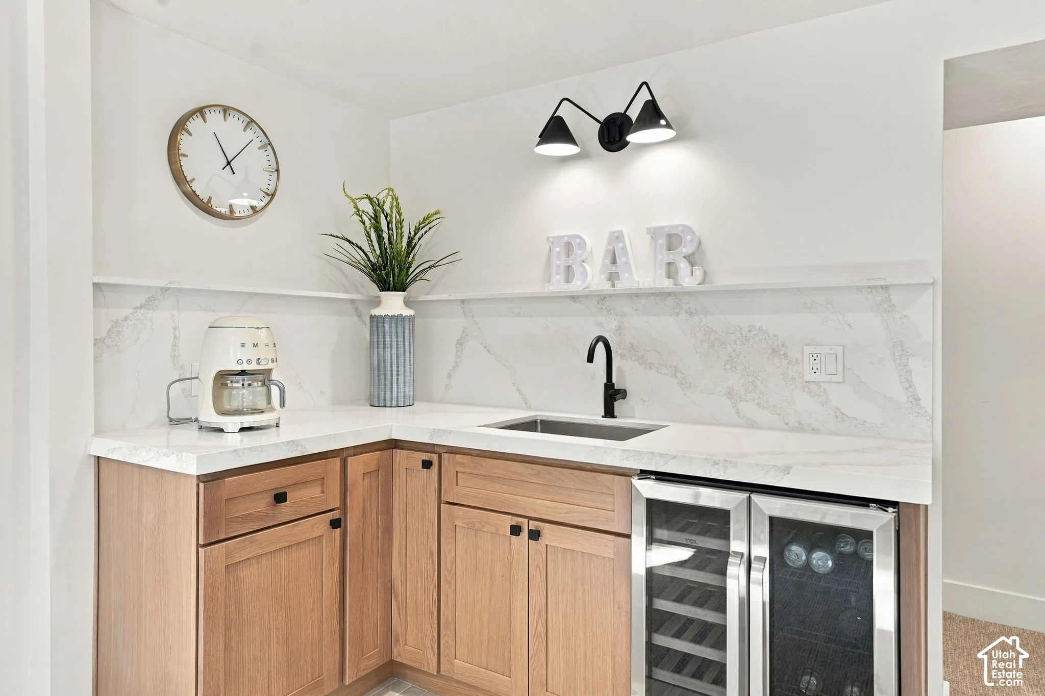 Corner wet bar featuring light wood-finish cabinetry, a white countertop, and a white and grey patterned backsplash