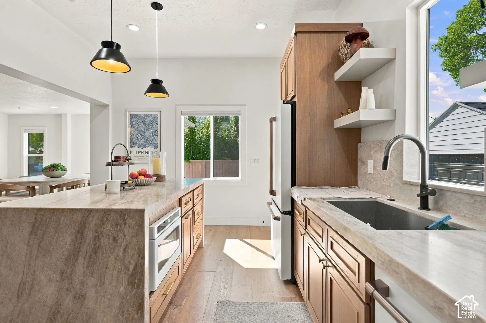 Kitchen featuring a waterfall island, built-in oven, pendant lighting, wood cabinetry, and a large window