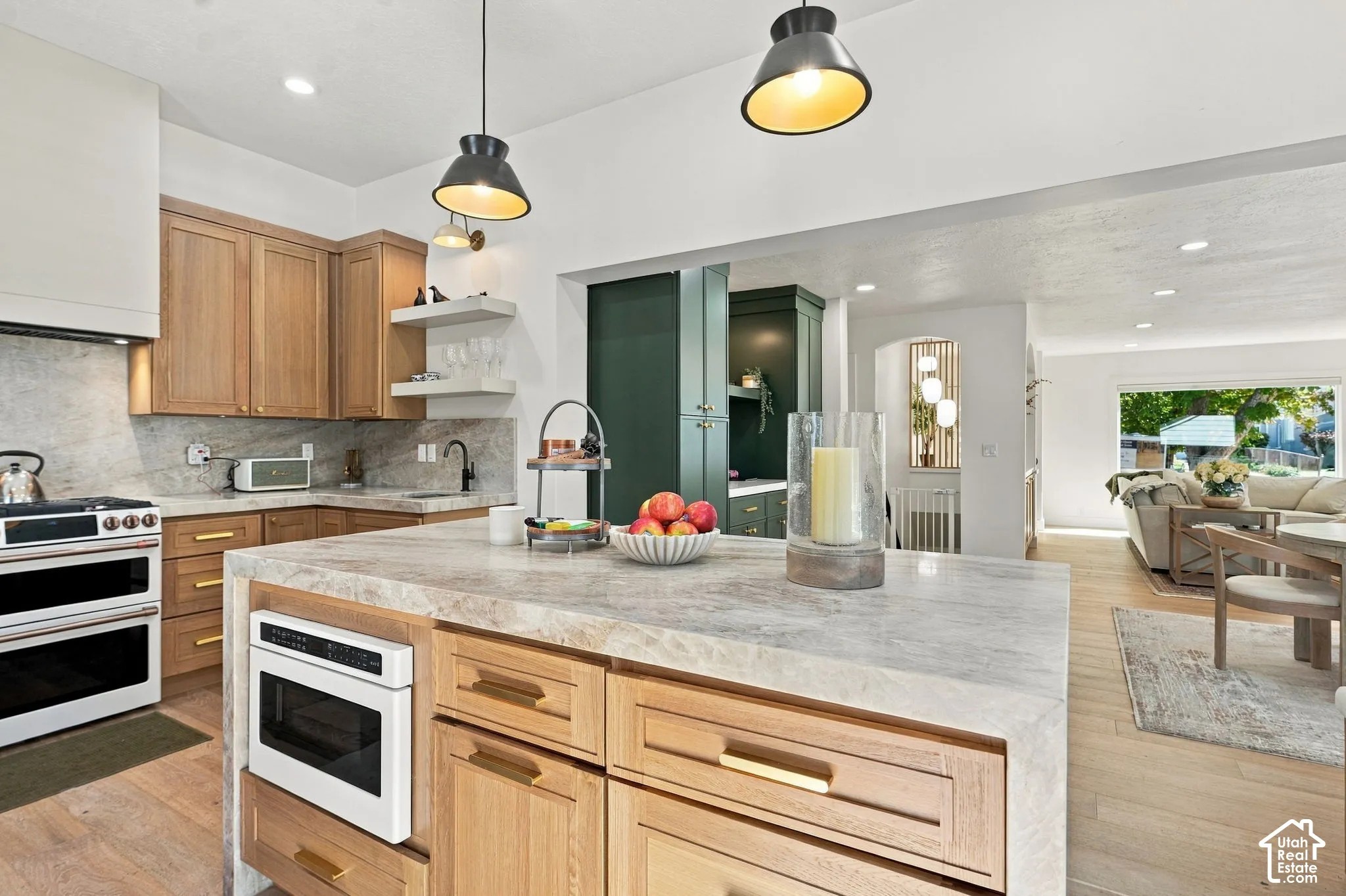 Kitchen featuring an oversized island with an integrated microwave, light wood-finish cabinetry, a white range with double ovens, and a natural stone backsplash and countertops