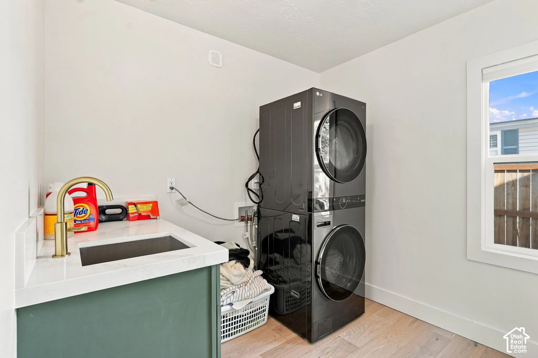 Laundry area featuring a built-in sink with a gold-finish faucet, white countertop, and stacked washer and dryer