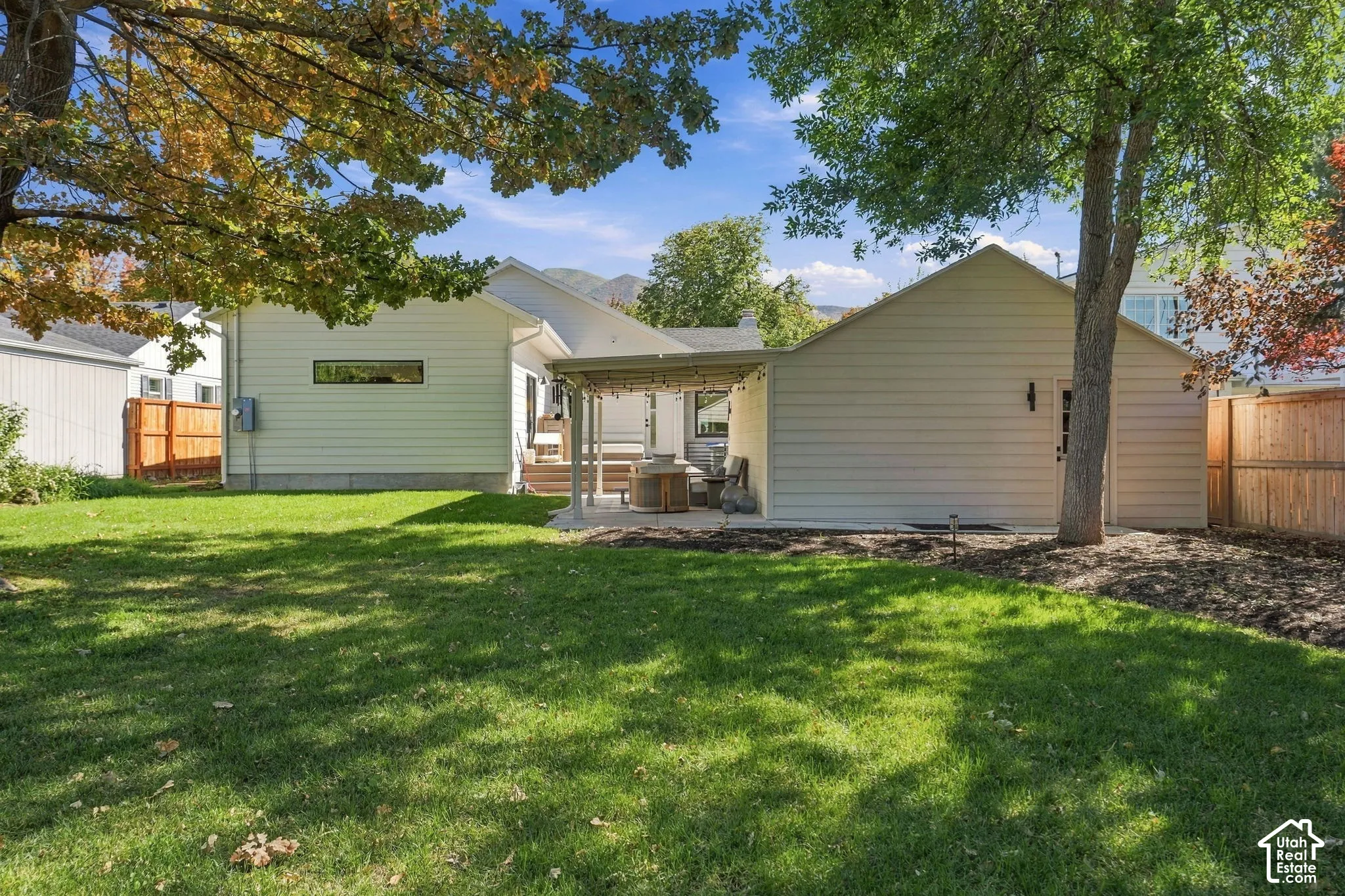Expansive backyard featuring a manicured lawn, established trees, and a covered patio area with a concrete surface