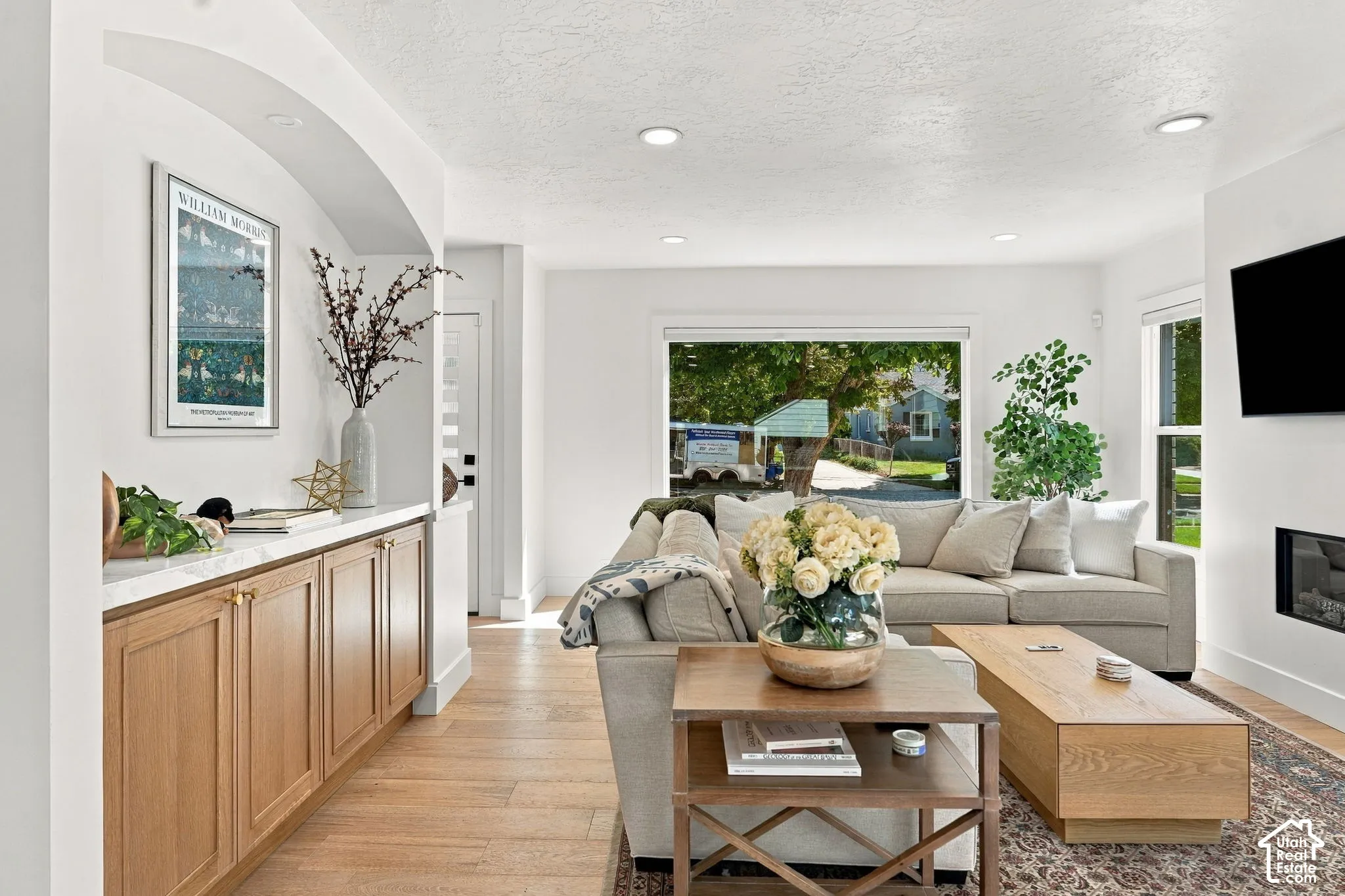 Recessed lighting illuminates the open living area featuring wood-finish flooring, a contemporary fireplace, and a large picture window