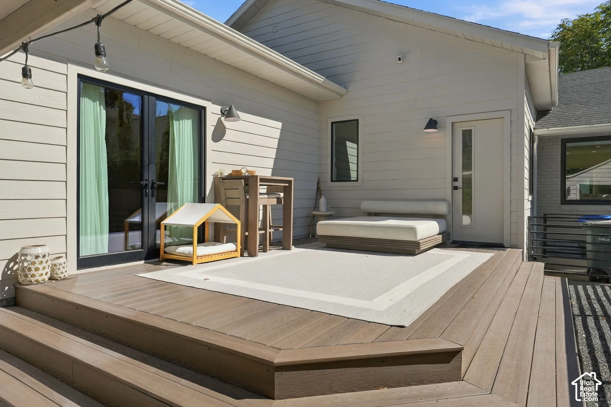 Expansive multi-level composite deck with wide steps and white siding, featuring black frame double patio doors and a single exterior door with a vertical glass panel