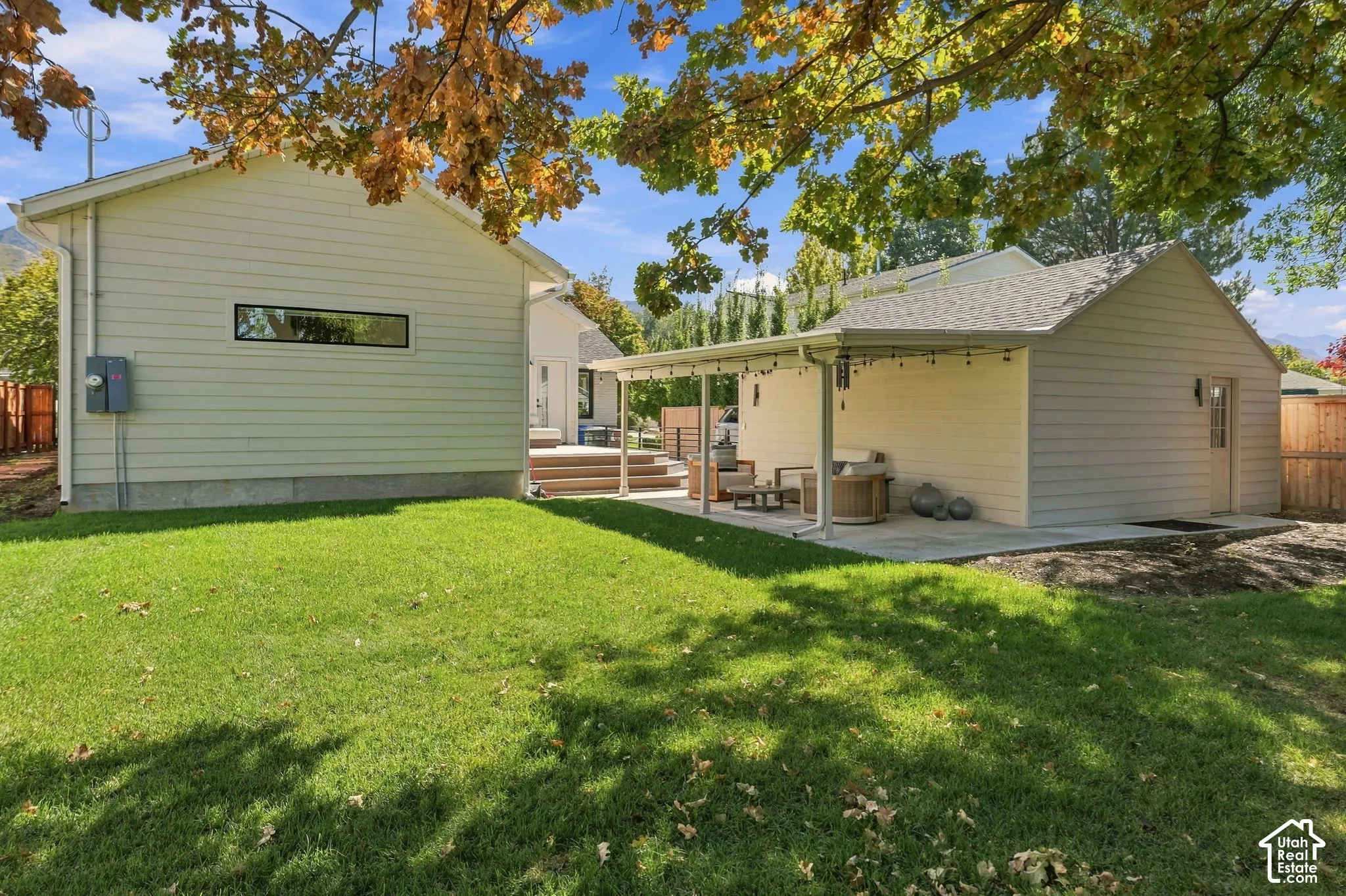 Expansive grass lawn, detached structure with horizontal siding and a horizontal window, covered patio area with string lighting, and a secondary structure with horizontal siding