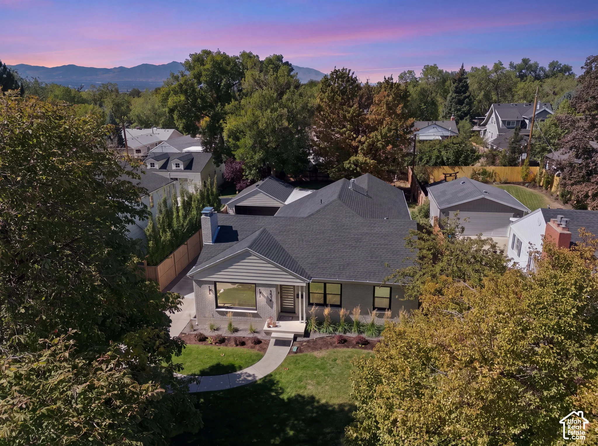 Gable roofline, landscaped front yard with mature trees, stone cladding, and a concrete pathway leading to the entry