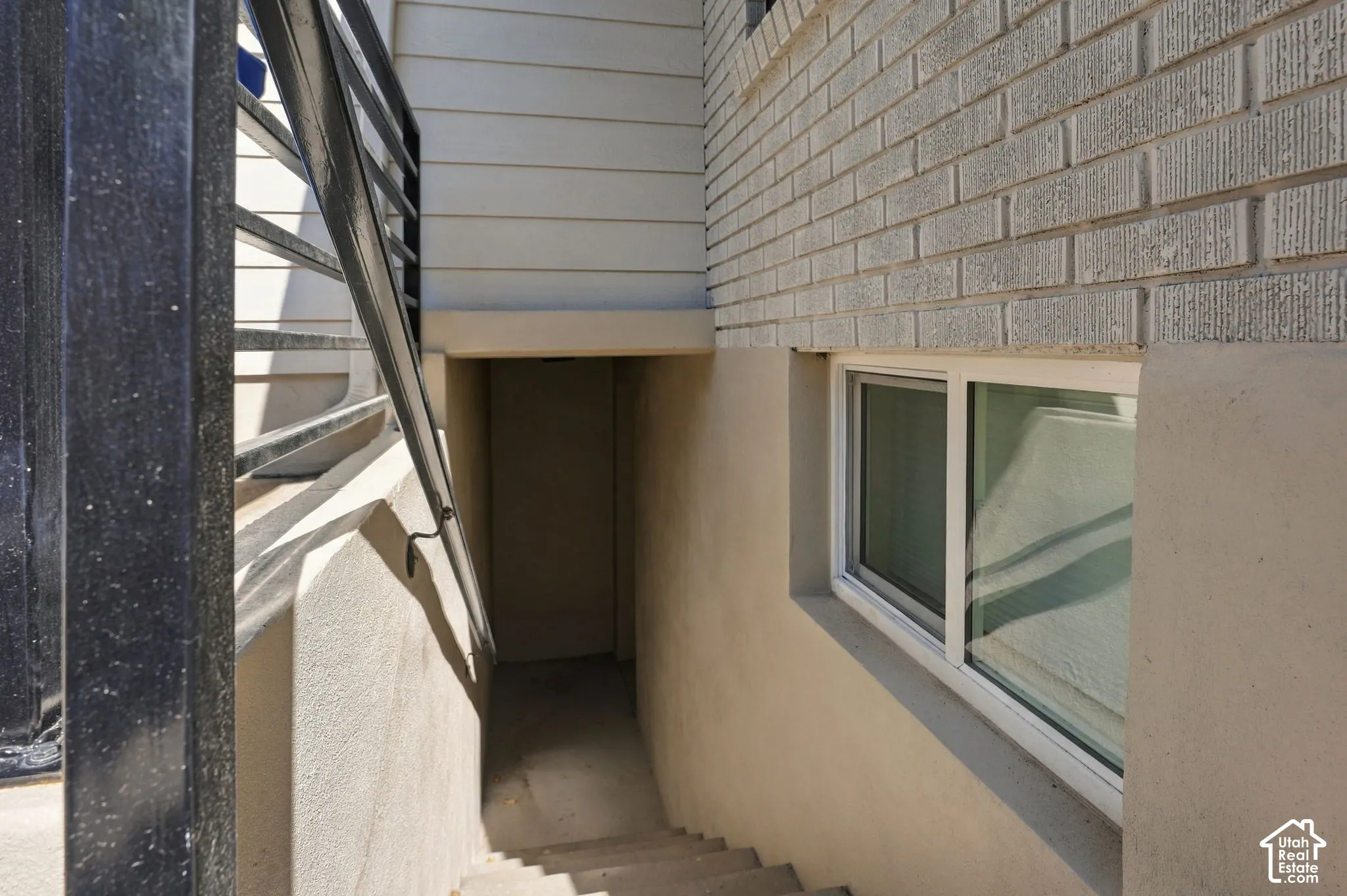 Concrete stairs leading to a recessed entrance, featuring a metal handrail and a white-framed window