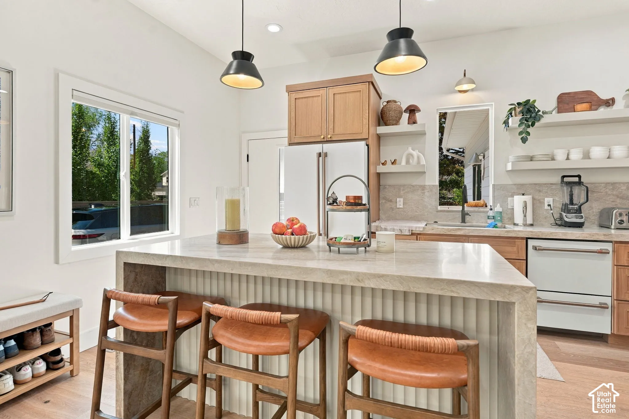 Kitchen featuring a large island with countertop seating, light wood cabinetry, stainless steel appliances, open shelving, and a window