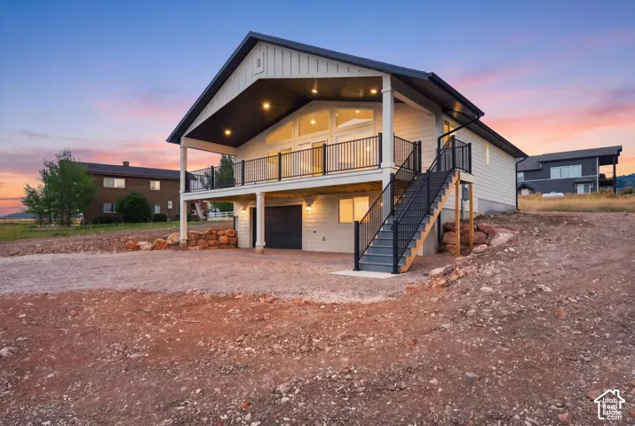 Modern exterior with board and batten siding, a covered balcony with metal railings, a ground-level garage door, and a prominent exterior staircase