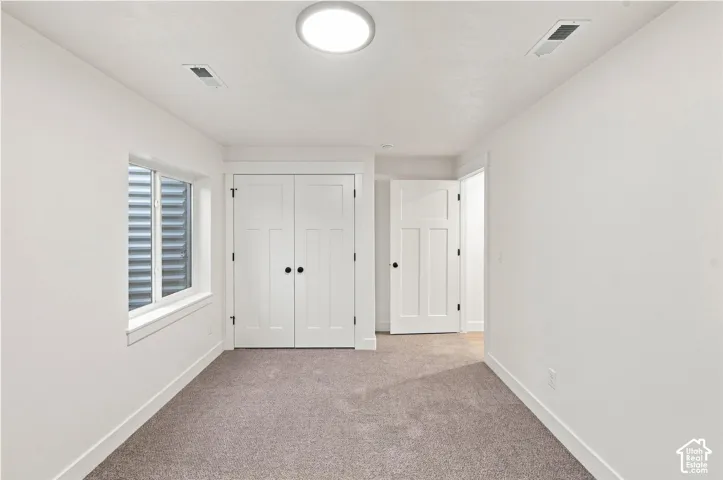 Carpeted room featuring a window with a window well, white walls, white doors, and a flush mount ceiling light