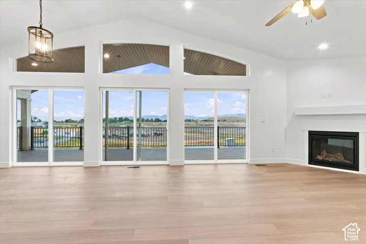 Vaulted ceiling great room featuring wood-finish flooring, a contemporary fireplace with a white mantel, and multiple sliding glass doors opening to an exterior deck